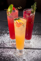 three glasses of fruit red yellow lemonade with ice in highball glasses on black background