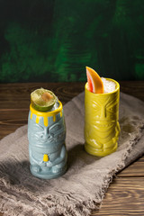 Tropical cocktails served in a tiki style glass and garnished with fruits on green wooden background