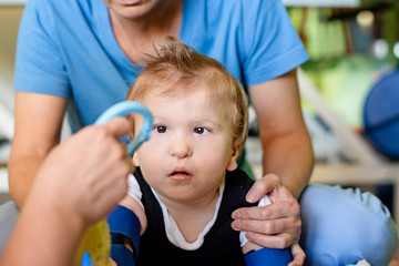 Portrait of a child with cerebral palsy on physiotherapy in a children therapy center. Boy with disability has therapy by doing exercises with physiotherapists in rehabitation centre.