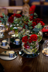 vertical photo of a wooden dining table decorated with bouquets of roses and candles