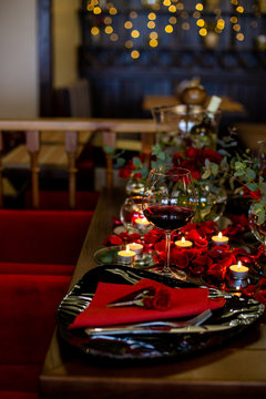 vertical photo of a glass of wine and a beautifully served plate surrounded by candles and rose petals