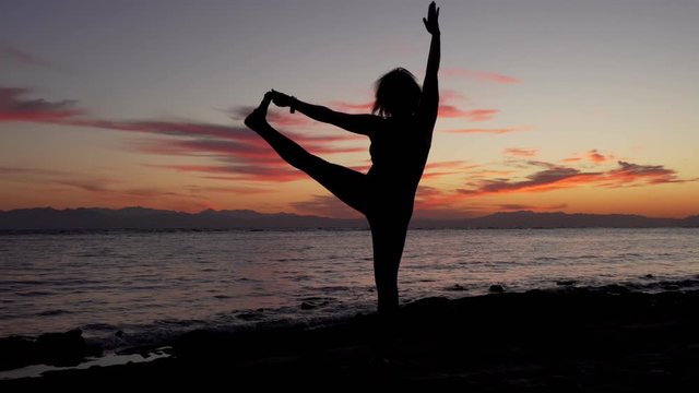 Silhouette of woman doing yoga extended hand-to-big-toe pose on sea sunset