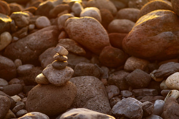 Balanced stone pyramide on shore of the ocean at dawn. Sea pebbles tower closeup symbolizing stability, zen, harmony, balance.