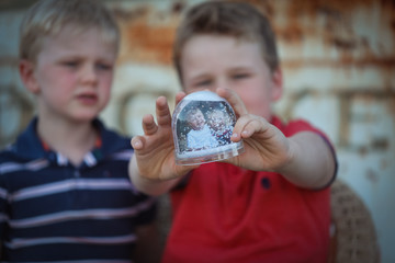 Two young brothers playing with Christmas themed snow globe featuring photos of themselves