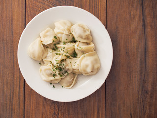 Portion of Russian traditional big size dumpling and herbs on a white plate and wooden table. Top view.