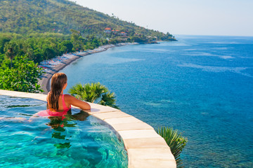 Happy girl have fun on summer beach holiday. Young woman relaxing at edge of infinity swimming pool with sea view from hill top. Healthy family lifestyle, summer travel with kids on tropical islands.