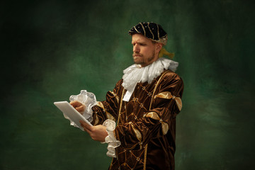 That's technology. Portrait of medieval young man in vintage clothing standing with tablet on dark...