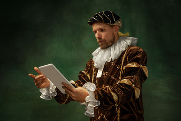 That's technology. Portrait of medieval young man in vintage clothing standing with tablet on dark...