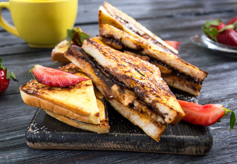 Sweet french toasts with banana, chocolate, strawberries on a wooden background. Tasty breakfast. Top view
