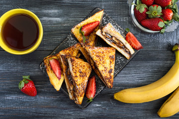 Sweet french toasts with banana, chocolate, strawberries on a wooden background. Tasty breakfast....