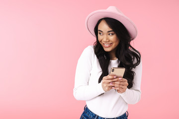 Image of young asian woman wearing hat smiling and holding cellphone