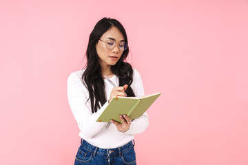 Image of young asian woman wearing eyeglasses making notes in diary book