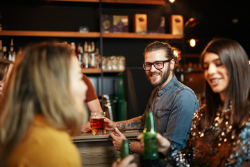 Group of friends drinking beer, chatting and having good time at pub. Night out.