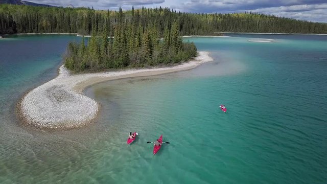 Kayakers Enjoy Kayaking In Caribbean Blue Water Near A Small Island Full Of Pine Trees During Sunny Day - Aerial shot