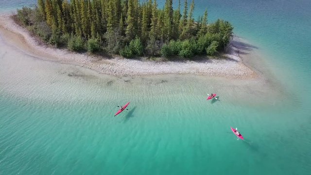 Tourists Kayaking In Caribbean Blue Water Near A Small Island In Boya Lake, British Columbia Canada - aerial shot