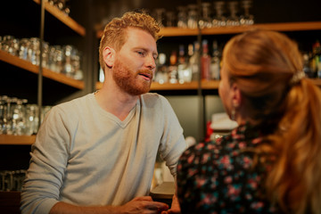 Handsome caucasian bearded ginger standing in bar with his female friend, drinking beer, chatting and having fun. Pub interior. Nightlife.