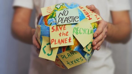 Man hands hold Earth globe with stickers with the message Save the Planet, Help, Recycling and No Plastic