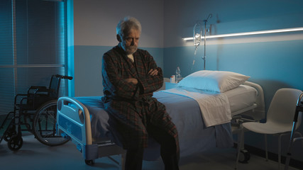 Depressed senior sitting on the hospital bed alone