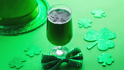 Happy Saint Patrick's Day greeting card with traditional symbols, shamrock, green attire. Green hat, bow tie, St Patricks Day shamrocks, golden confetti on green background, copy space