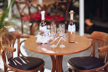 Wedding decorations for the newlyweds. Two decorated bottles, in the form of a bride and groom, glasses with ribbons stand on a wooden table. Photography, concept, composition.