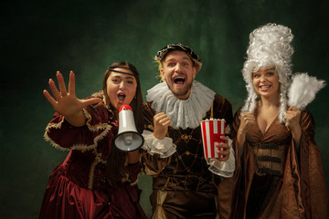 Real sport fans. Portrait of medieval young people in vintage clothing on dark background. Models...