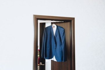 Blue men's jacket hanging on a hanger against the background of a white wall. Morning and...