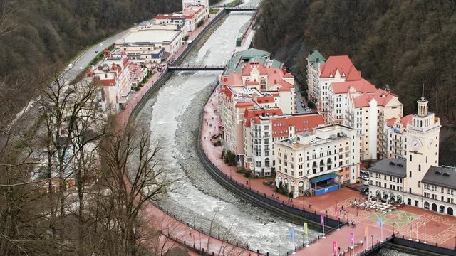Aerial view of a village located by the mountains covered by bald trees. Stock footage. Flying above beautiful village and fast river flowing along the brick houses.