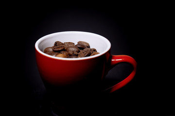 Coffee beans in a red cup on a black background. Photo in the dark