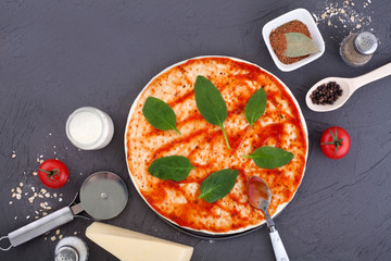 Ingredients for pizza, including the dough close-up smeared with ketchup, decorated with spinach, a knife for cutting round, on a gray background. The concept of making pizza.