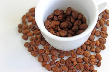 Spilled coffee beans from the white ceramic cup isolated on white background