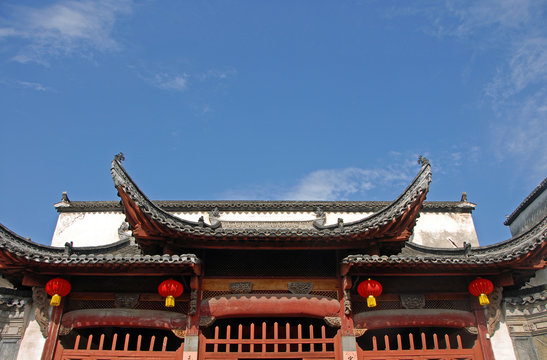 Xidi Ancient Town in Anhui Province, China. Zhuimu Tang is a hall in the old town of Xidi. Image shows the traditional Chinese roof set against the blue sky and red lanterns. Hall in Xidi ancient town