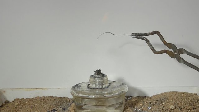 A strip of magnesium band burns with a bright white flame, the item is held in  forceps, magnesium is a metal that can easily burn.