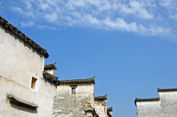 Xidi Ancient Town in Anhui Province, China. Traditional roofs and white walls in the old town of Xidi set against a blue sky. Tiles and eaves of old roofs in the historical town of Xidi in China. 