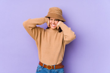 Young caucasian woman isolated on purple background covering ears with hands.
