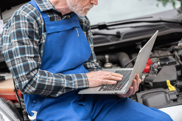 Mechanic using laptop for checking car engine