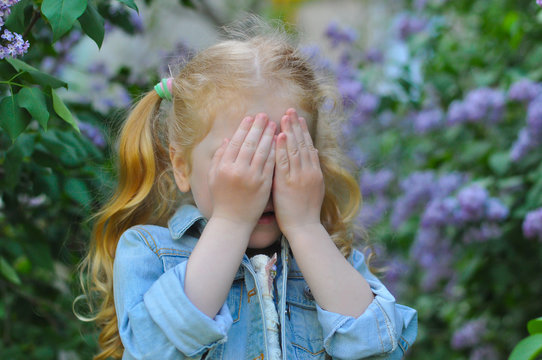 horizontal closeup photo of a little girl who is playing hide and seek in a flowering garden