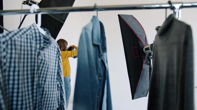 Backstage of photoshoot in modern photo studio: handsome young man is posing for photographer with camera, hanger with trendy clothing is visible.