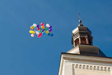 Balony na niebieskim niebie lecą obok wieży kościoła