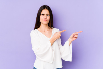 Young caucasian woman isolated on purple background shocked pointing with index fingers to a copy space.
