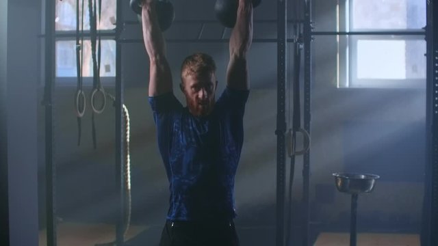 Athletic strong male using two kettlebell for fitness workout, in slow motion. cross-training.