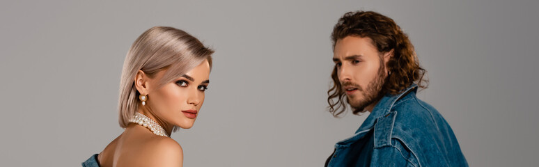 panoramic shot of stylish man in denim jacket looking at attractive woman isolated on grey