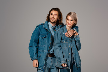 smiling man hugging woman in denim jacket isolated on grey