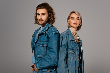 Fototapeta premium back to back view of stylish man and woman in denim jackets looking at camera isolated on grey