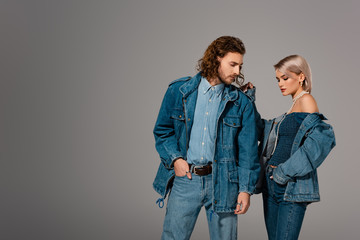 stylish man and woman in denim jackets looking down isolated on grey