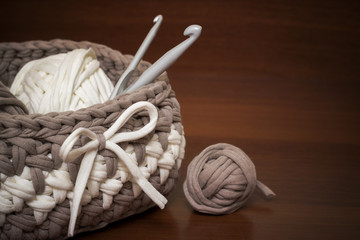 Knitted basket of handmade knitted yarn on a wooden background. In the basket are balls of knitted...
