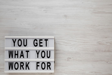 'You get what you work for' words on a modern board on a white wooden background, top view. Overhead, from above, flat lay. Copy space.