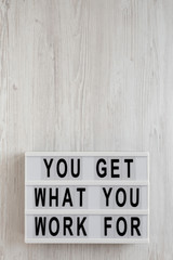 'You get what you work for' words on a modern board on a white wooden background, overhead view. Top view, from above, flat lay. Copy space.