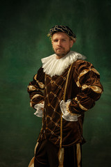 Posing thoughtful. Portrait of medieval young man in vintage clothing standing on dark background....