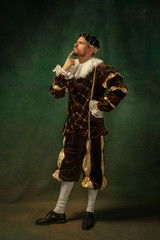 Posing thoughtful. Portrait of medieval young man in vintage clothing standing on dark background....