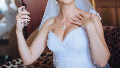 A beautiful and gentle bride clicks on a perfume bottle. Tasty and stylish aroma. Morning and preparation of the bride. Photography, concept.
